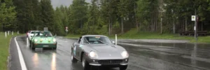 Ferrari und Porsche Oldtimer bei der Kitzbüheler Alpenrallye auf einer regennassen Alpenstraße vor Bergkulisse